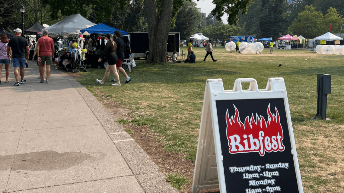 ribfest sign in foreground on a path in London Ontario with tents in the background and some plastic bubble soccer bubbles in an open park field that kids are playing in