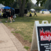 ribfest sign in foreground on a path in London Ontario with tents in the background and some plastic bubble soccer bubbles in an open park field that kids are playing in