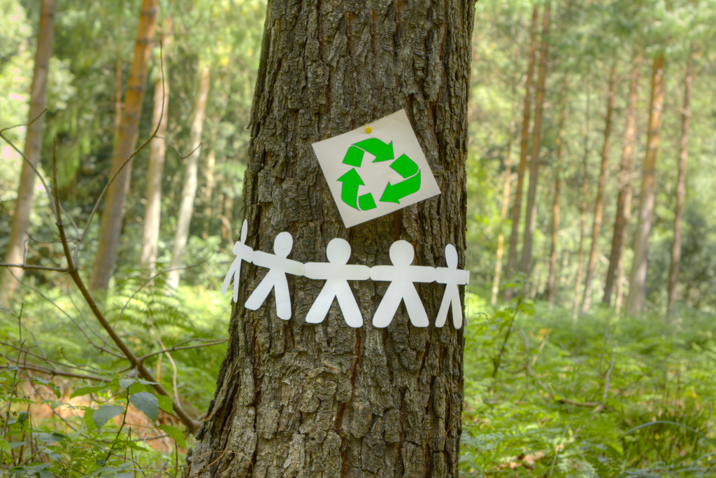 Green recycle sign with paper men holding hands on a tree.