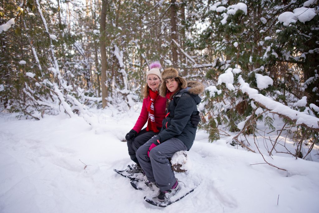 mother_daughter_seated_in_woods_wearing_snowshoes