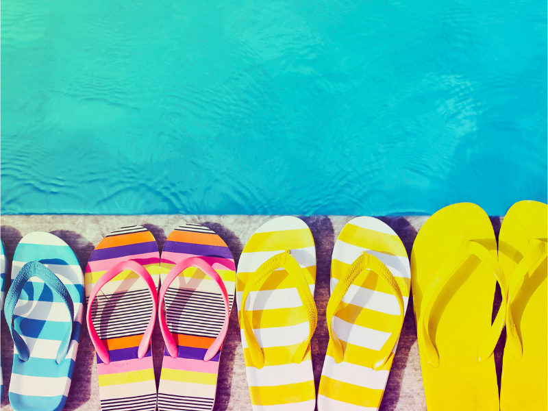 four pairs of colourful flip flops on pool deck
