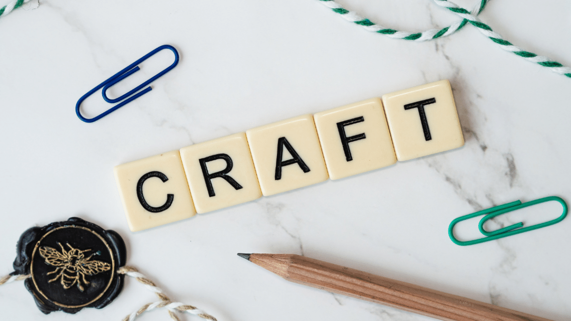 craft spelled out in scrabble letters with blue paper clip in the distance and a bit of string on a countertop that is white and looks like marble