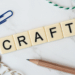 craft spelled out in scrabble letters with blue paper clip in the distance and a bit of string on a countertop that is white and looks like marble