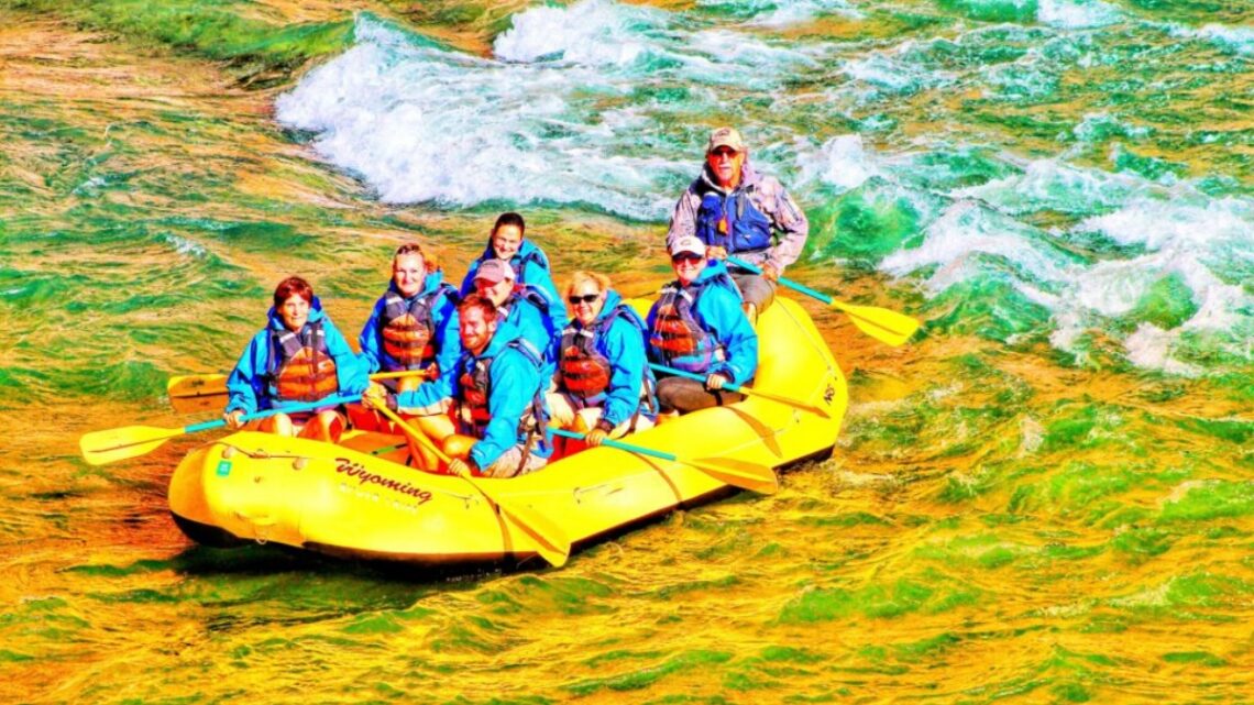 8 people in a yellow raft white water rafting in Cody Wyoming down the Shoshone River. All are wearing some blue wet jacket gear and life jackets