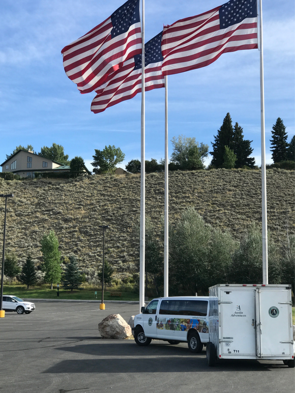 Austin Adventures shuttle parked in Cody Wyoming beneath two large American flags