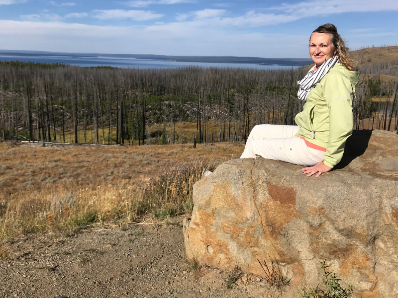 woman in green jacket sitting on a rock looking out at Yellowstone Lake in Yellowstone National Park on a group travel tour