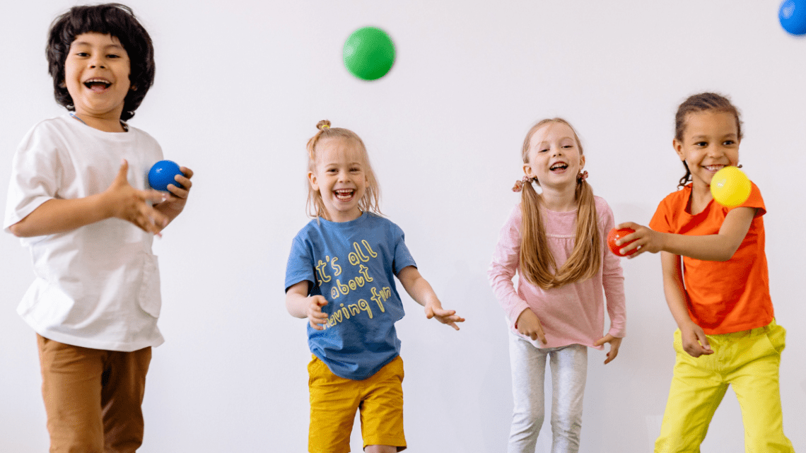 four young kids playing ball indoors and laughing