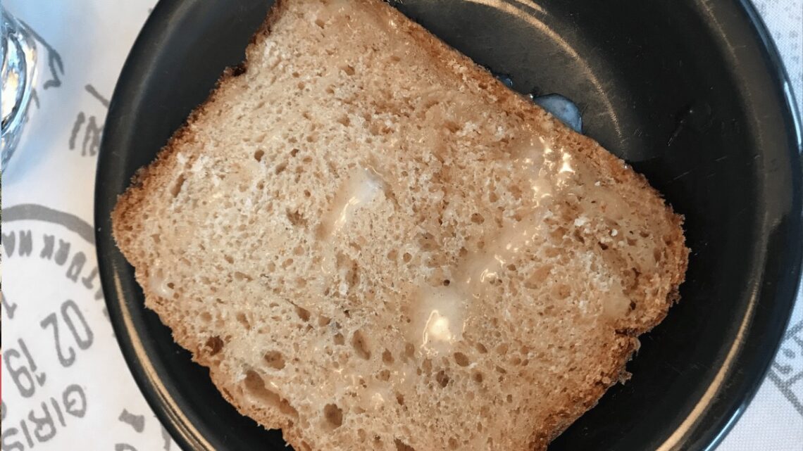 glazed apple bread made in bread maker and sitting on a black plate with some melted butter on the slice of moist brown bread