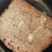 glazed apple bread made in bread maker and sitting on a black plate with some melted butter on the slice of moist brown bread