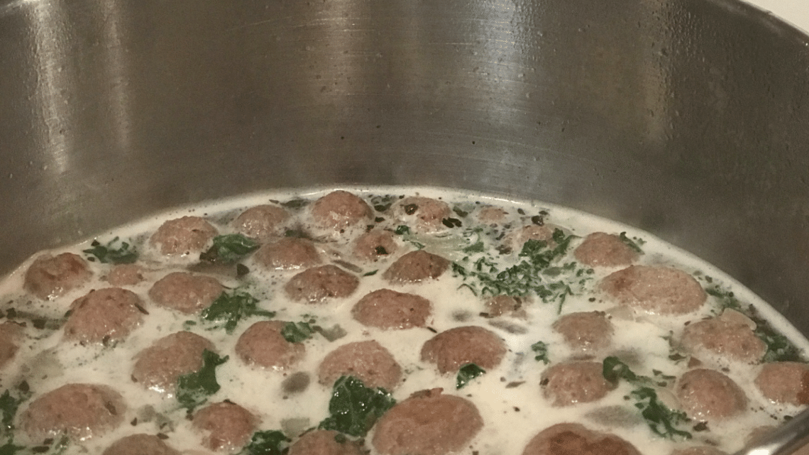 Italian wedding soup meatballs boiling in a large pot on the stove