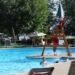 big public pool deck at a resort with colourful umbrellas and a life guard chair. several people of all ages are in the pool and it is a sunny day