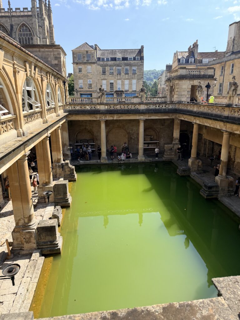 roman baths in bath England, open building overlooking a green coloured long rectangular bath