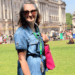 woman in a denim dress standing in front of Buckingham palace wearing the sunflower lanyard and smiling with bright pink tote bag purse