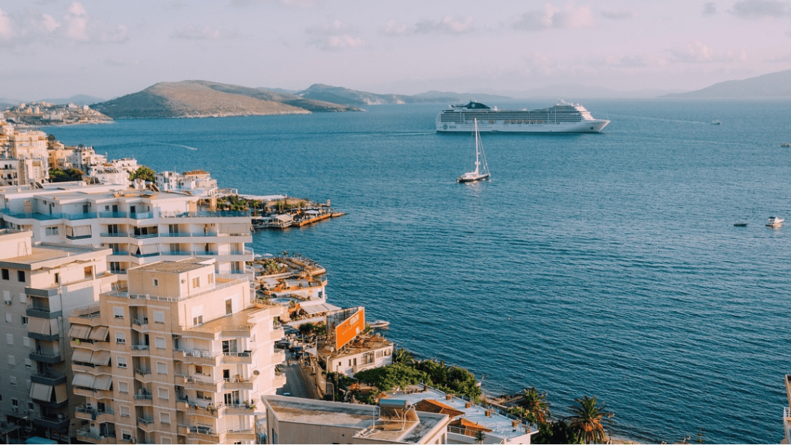 cruise boat in a very blue sea, sailboat in front of the ship and gorgeous Mediterranean looking buildings in the foreground.