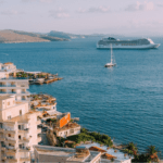 cruise boat in a very blue sea, sailboat in front of the ship and gorgeous Mediterranean looking buildings in the foreground.