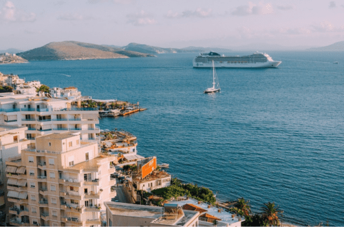 cruise boat in a very blue sea, sailboat in front of the ship and gorgeous Mediterranean looking buildings in the foreground.