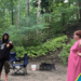 sable beach camping at provincial park trees in the background and two young adults in front of a tent. One is in black and covered and getting ready to start a fire